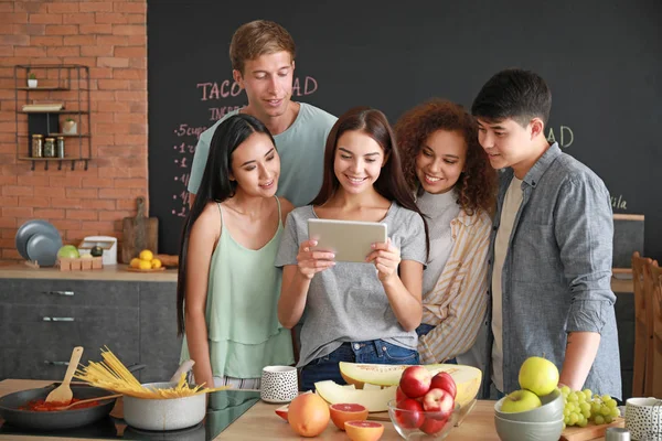 Happy friends with tablet computer searching recipe while cooking together in kitchen — Stock Photo, Image