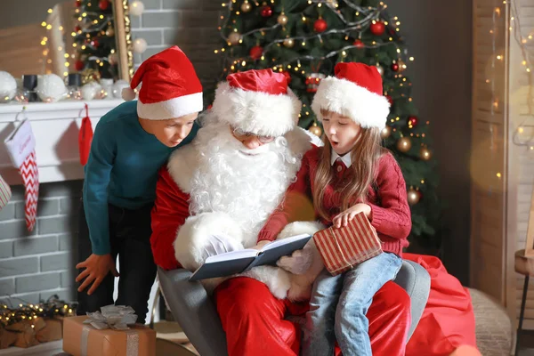 Jultomten och små barn läser bok i rummet dekorerad för julen — Stockfoto