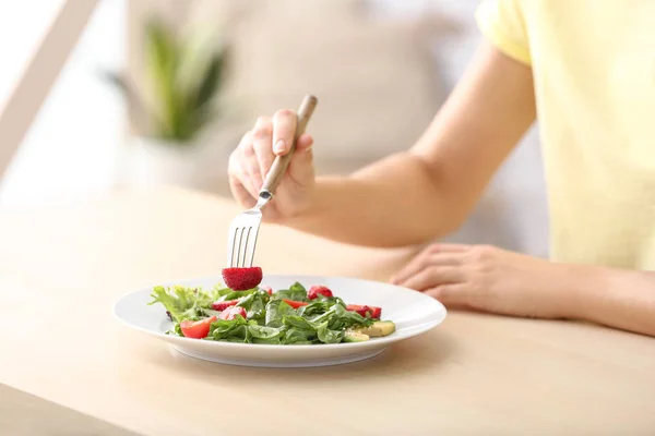 Mulher comendo salada fresca com morango e espinafre à mesa — Fotografia de Stock