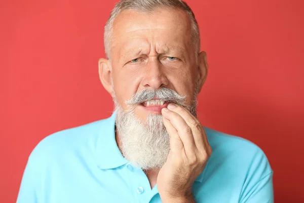 Senior man suffering from toothache against color background — Stock Photo, Image