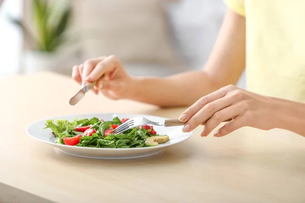 Mulher comendo salada fresca com morango e espinafre à mesa — Fotografia de Stock