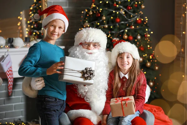 Santa Claus and little children with gifts in room decorated for Christmas — Stock Photo, Image