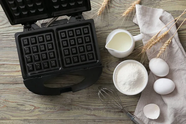 Modern waffle maker with ingredients on wooden table — Stock Photo, Image