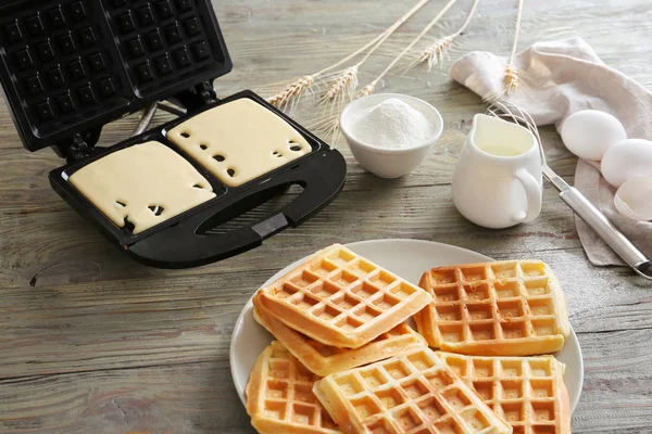 Modern maker with waffles and ingredients on wooden table — Stock Photo, Image