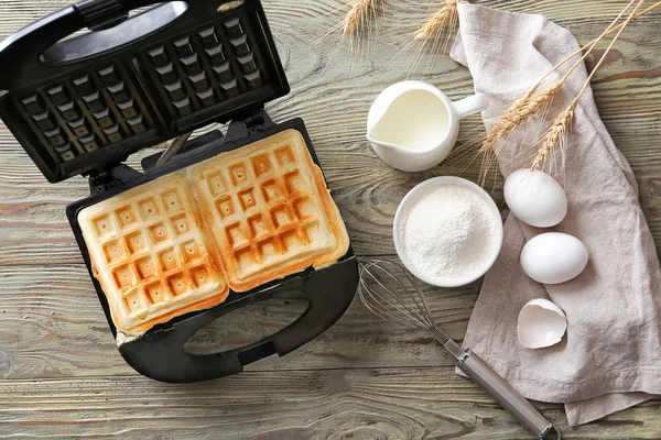 Modern maker with waffles and ingredients on wooden table — Stock Photo, Image