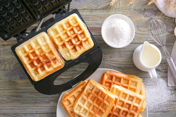 Modern maker with waffles and ingredients on wooden table — Stock Photo, Image