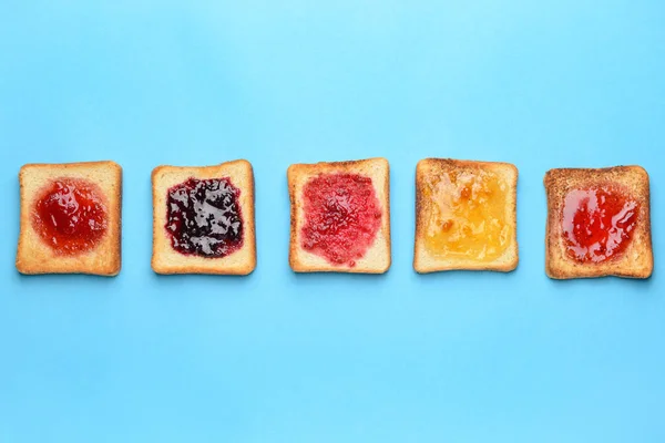 Tasty toasted bread with different jams on color background — Stock Photo, Image