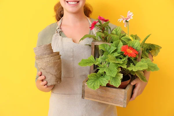 Female gardener with flowers on color background — Stock Photo, Image