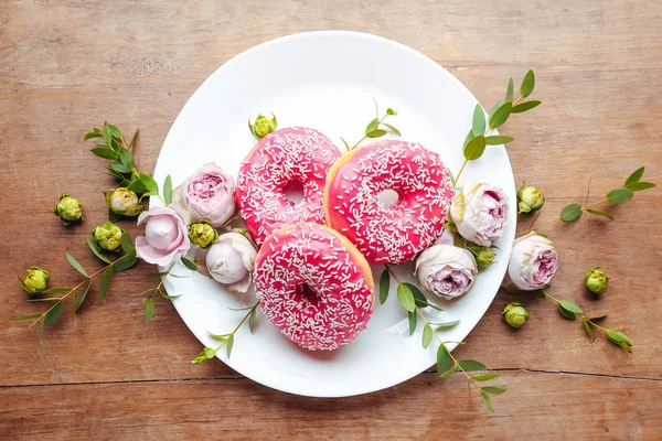 Plate with sweet tasty donuts and flowers on table — Stock Photo, Image