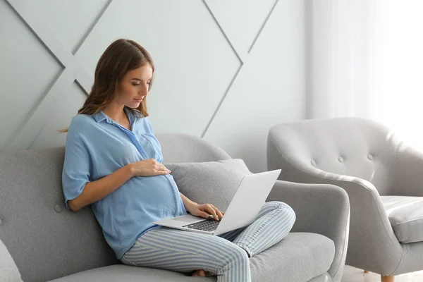 Beautiful pregnant woman with laptop sitting on sofa at home — Stock Photo, Image