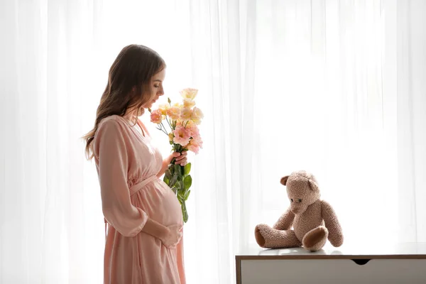 Mujer embarazada hermosa con flores cerca de la ventana — Foto de Stock