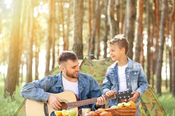 Padre e il suo piccolo figlio con la chitarra fare picnic nella foresta — Foto Stock