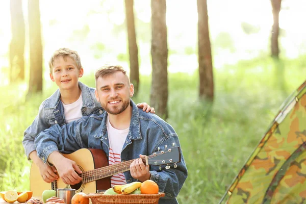 Father and his little son with guitar having picnic in forest — Stock Photo, Image