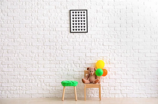 Cadeira com urso de brinquedo, balões e banquinho perto da parede de tijolo branco no quarto das crianças — Fotografia de Stock