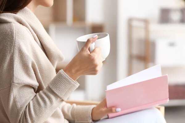Beautiful young woman drinking tea while reading book at home