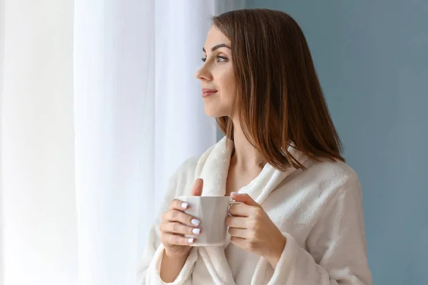 Beautiful young woman drinking tea near window — Stock Photo, Image