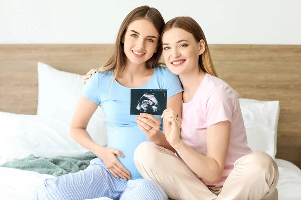 Беременная лесбийская пара с изображением УЗИ в спальне — стоковое фото