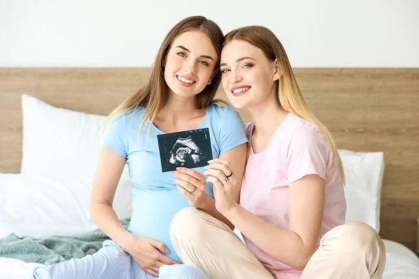 Pareja lesbiana embarazada con imagen de sonograma en el dormitorio — Foto de Stock
