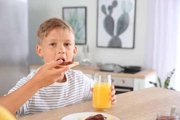 Funny little boy eating tasty toasts with jam in kitchen — Stock Photo, Image