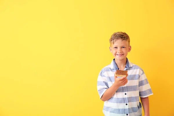 Funny little boy holding tasty toast with chocolate spreading on color background — Stock Photo, Image