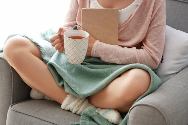 Jovem com livro bebendo chá quente em casa — Fotografia de Stock