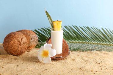 Kum üzerinde lezzetli Pina Colada kokteyl, hindistan cevizi, çiçek ve tropikal yaprak Cam