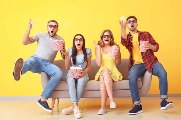 Emotional friends with popcorn watching movie on sofa near color wall — Stock Photo, Image