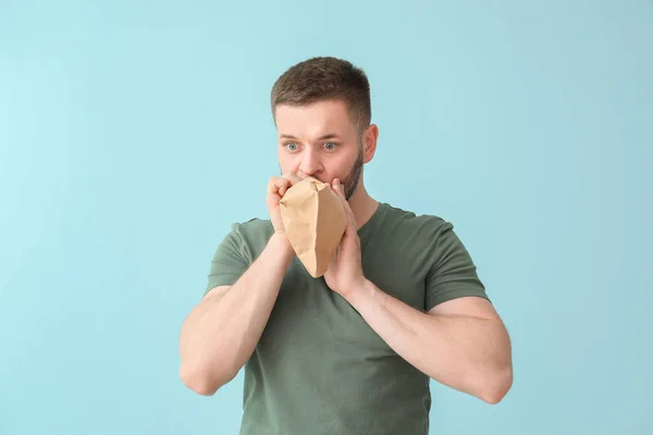 Uomo con sacchetto di carta con attacco di panico sullo sfondo di colore — Foto Stock