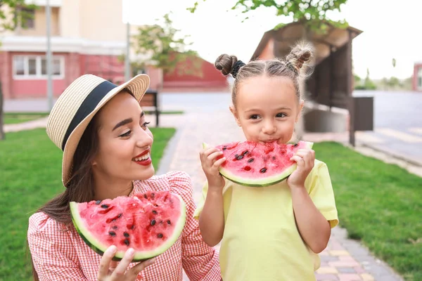 Cute little girl and her mother eating sweet watermelon in park