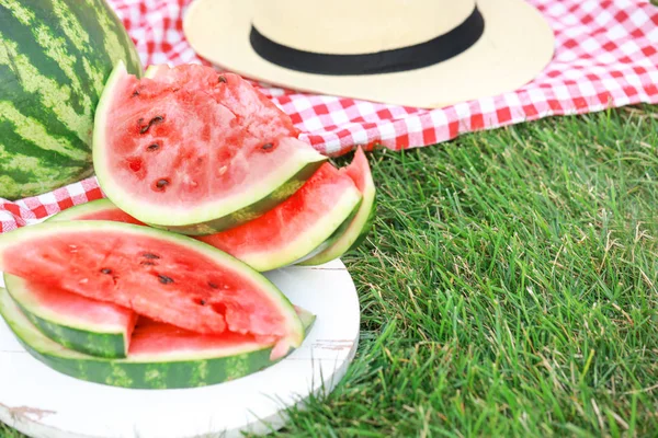 Fresh cut watermelon and hat on green grass outdoors