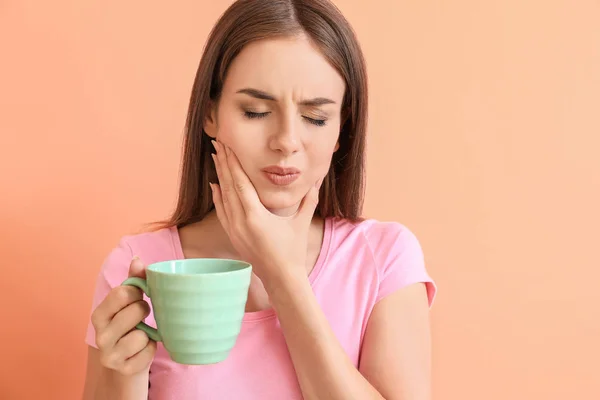 Mujer joven con dientes sensibles y taza de café caliente sobre fondo de color — Foto de Stock