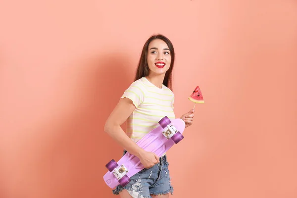 Beautiful young woman with slice of fresh watermelon and skateboard on color background — Stock Photo, Image