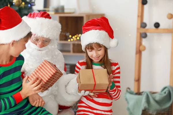 Santa Claus and his little helpers with gifts in room decorated for Christmas — Stock Photo, Image
