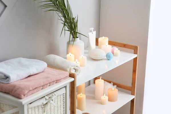Beautiful burning candles and cosmetics on stand in bathroom — Stock Photo, Image