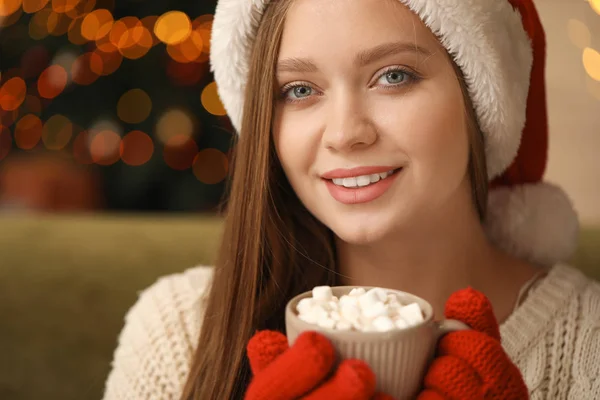美丽的女人在圣诞老人帽子喝热巧克力在家里 — 图库照片