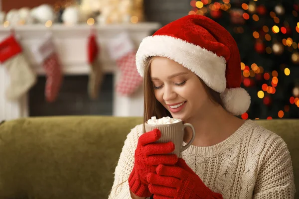 Schöne Frau mit Weihnachtsmann-Hut, die zu Hause heiße Schokolade trinkt — Stockfoto