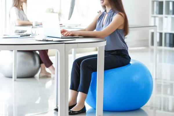 Young businesswoman sitting on fitball while working in office — Stock Photo, Image