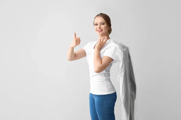 Frau mit Kleidung nach der Reinigung zeigt Daumen nach oben auf hellem Hintergrund — Stockfoto