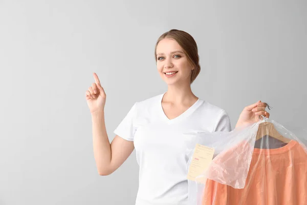 Vrouw met kleren na drogen-reiniging wijzend op iets op lichte achtergrond — Stockfoto
