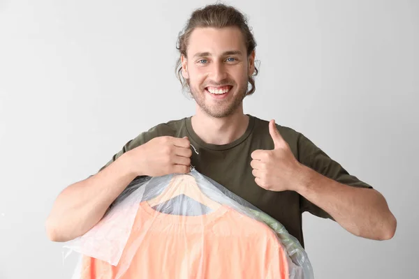 Man with clothes after dry-cleaning showing thumb-up on light background — Stock Photo, Image