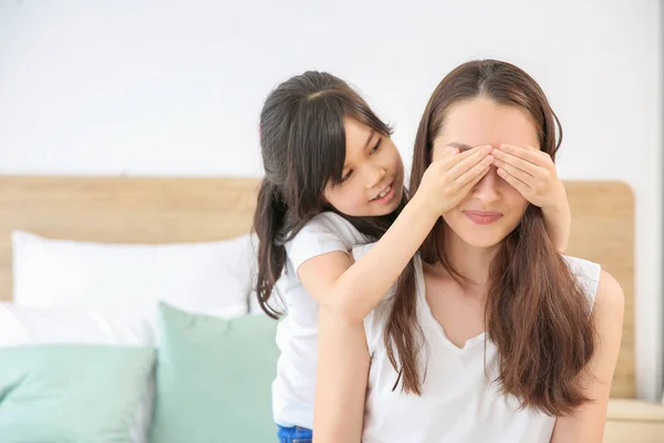 Little girl covering eyes of her mother in bedroom — Stock Photo, Image