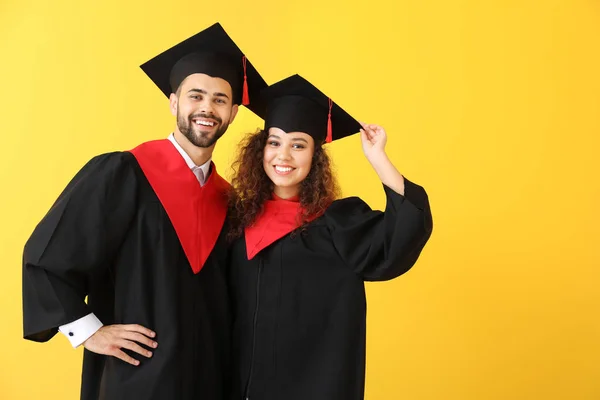 Young students in bachelor robes on color background