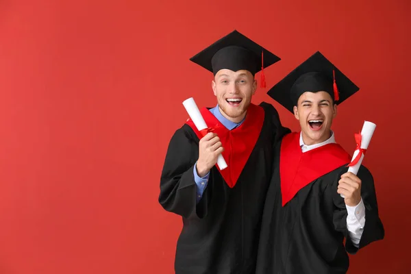 Happy students in bachelor robes on color background — Stock Photo, Image