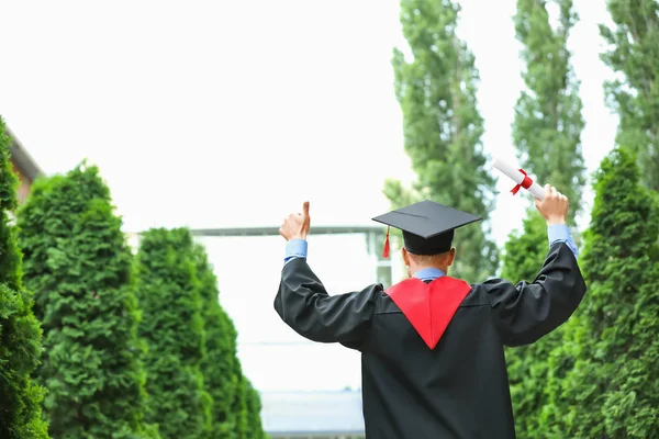 Szczęśliwy młody student w kawalerskie szaty i dyplom na dworze — Zdjęcie stockowe