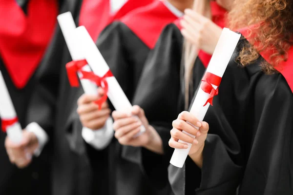 Jovens estudantes em roupões de solteiro e com diplomas ao ar livre — Fotografia de Stock