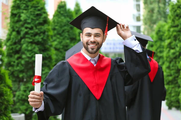 Чоловік студент в холостяцькому халаті і з дипломом на відкритому повітрі — стокове фото