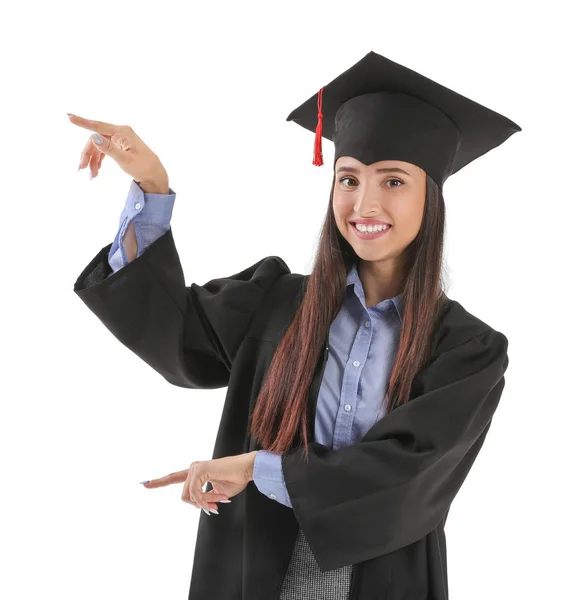 Estudante feminina em boné de formatura e vestido apontando para algo no fundo branco — Fotografia de Stock