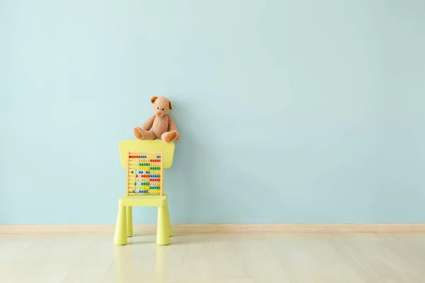 Silla con oso de peluche y ábaco cerca de la pared de color en la habitación de los niños — Foto de Stock