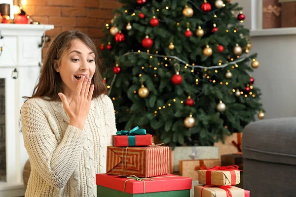 Surprised young woman with Christmas gifts at home — Stock Photo, Image