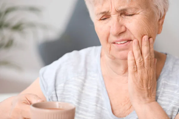 Senior woman with sensitive teeth and cup of hot coffee at home — Stock Photo, Image